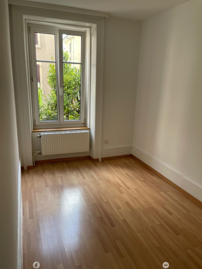 Empty room with wooden flooring, white walls, and a large window with a radiator below it.