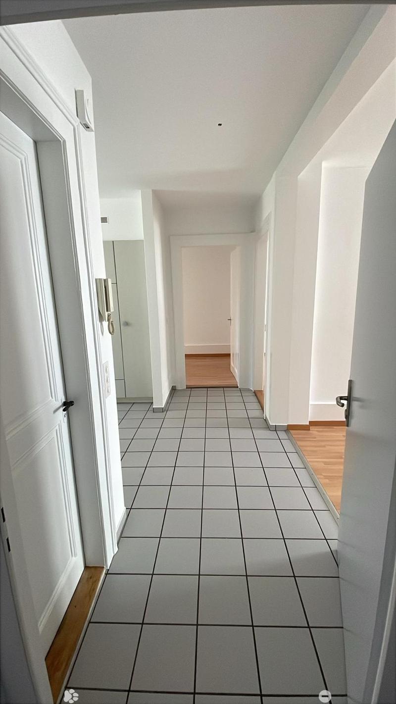 A clean, well-lit hallway with tiled flooring and white walls, featuring several doors and a telephone on the wall.