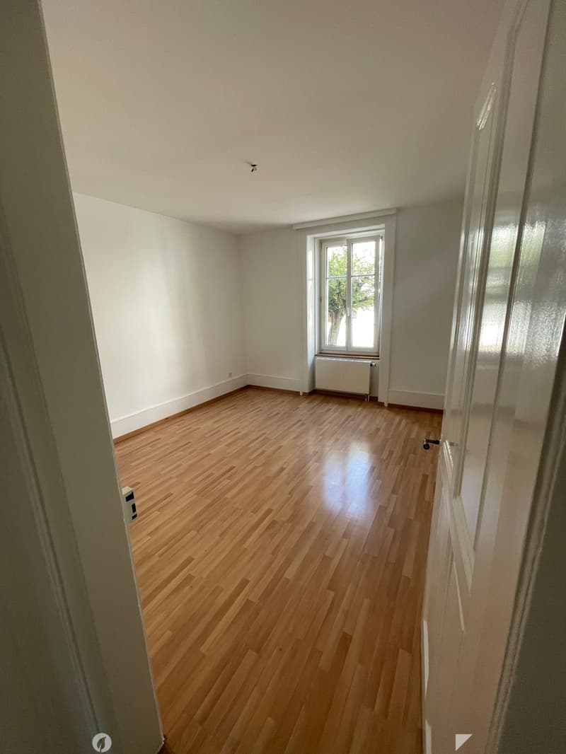 Empty room with wooden flooring, white walls, and a window with a radiator below it.