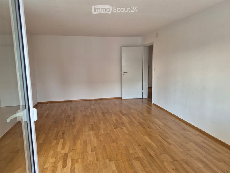 Empty room with wooden flooring and white walls, featuring a door and a large window with blinds.