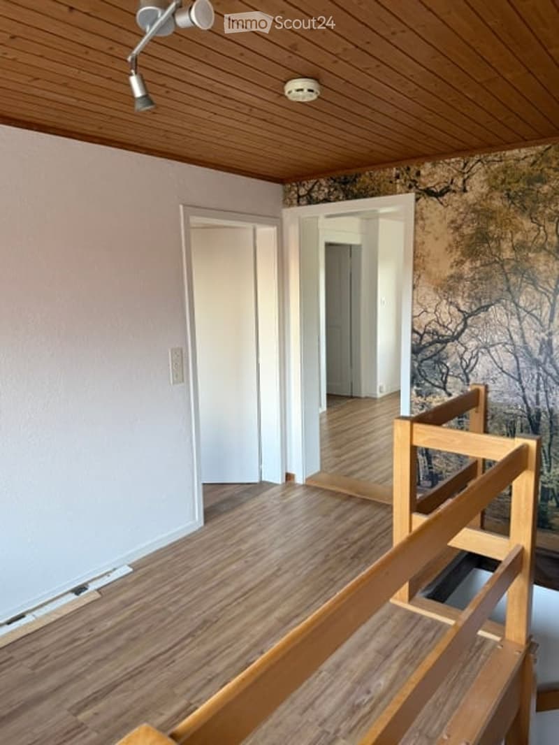 Empty room with wooden flooring, white walls, and a wooden railing leading to another room. No furniture or equipment is present.