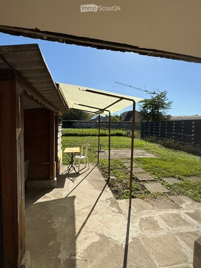 Outdoor patio area with a small table and chairs, surrounded by a fence and grassy yard, under a clear blue sky.