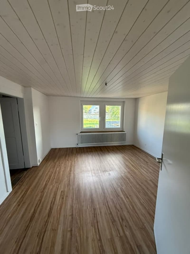 Empty room with wooden flooring, white walls, and a radiator under a window. No furniture or equipment present.