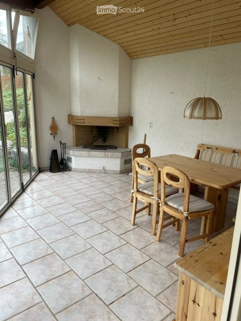 Bright room with wooden ceiling, fireplace, large windows, wooden dining table and chairs, wooden bench, and wooden cabinet.