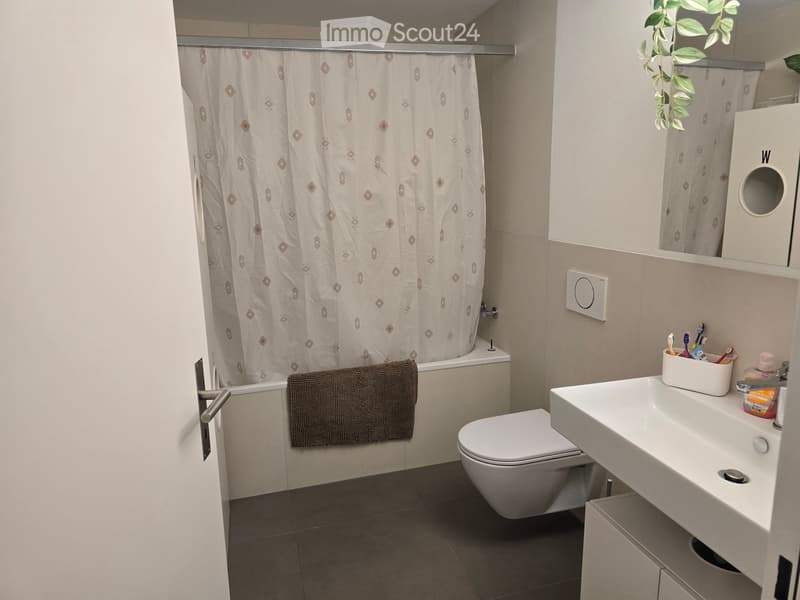 Modern bathroom with a bathtub, toilet, sink, and a towel hanging on the side. The shower curtain has a diamond pattern, and a toothbrush holder is on the sink.