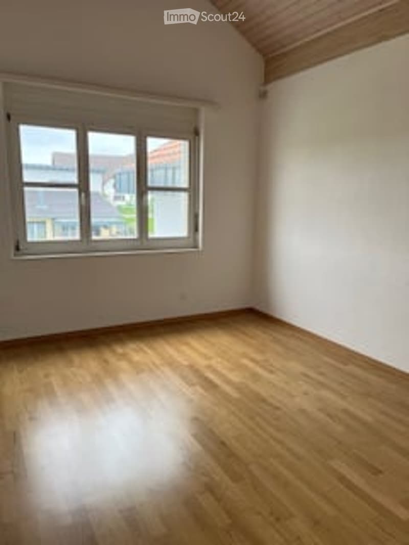 Spacious bedroom with hardwood flooring, white walls, and large windows providing natural light.