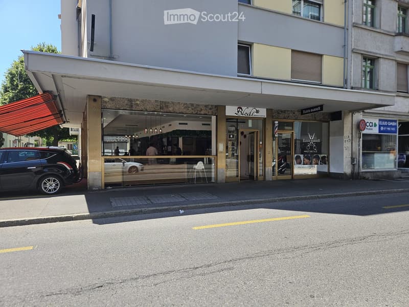 Multi-story commercial building with storefronts, including a barbershop and a restaurant, with glass windows and awnings.