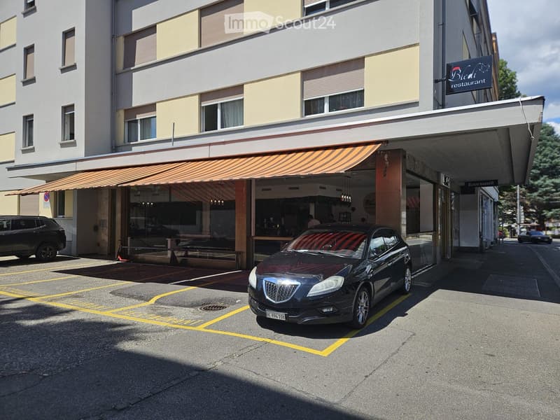 Two-story building with a restaurant sign, striped awning, and parked cars in front.