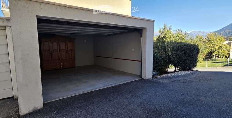 Garage with a wooden wardrobe inside, surrounded by greenery and a clear blue sky with mountains in the background.
