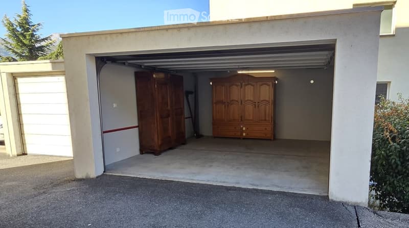 Garage with two large wooden wardrobes inside, concrete floor, white walls, and a partially open door.