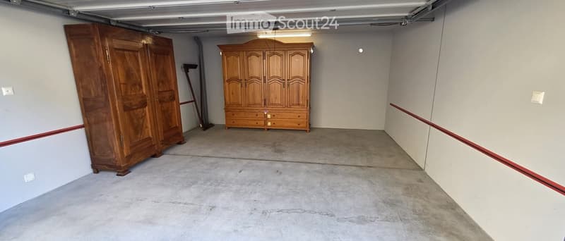 Garage with a large wooden wardrobe and a wooden cabinet, concrete floor, and overhead garage door.