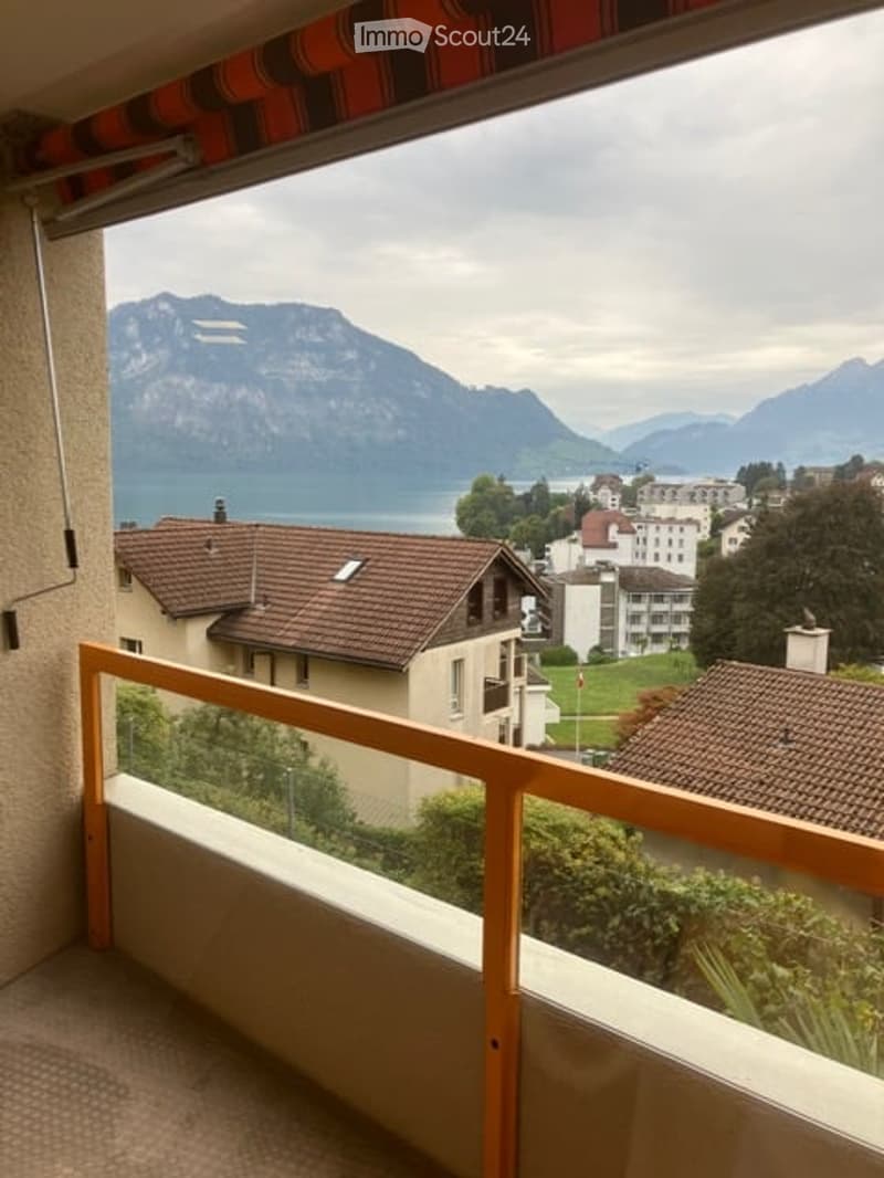 Balcony with wooden railing, overlooking a scenic lake and mountain landscape.