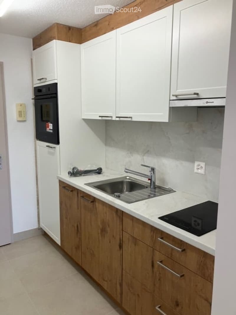Modern kitchen with white cabinets, wooden lower cabinets, stainless steel sink and faucet, built-in oven, and electric stovetop.