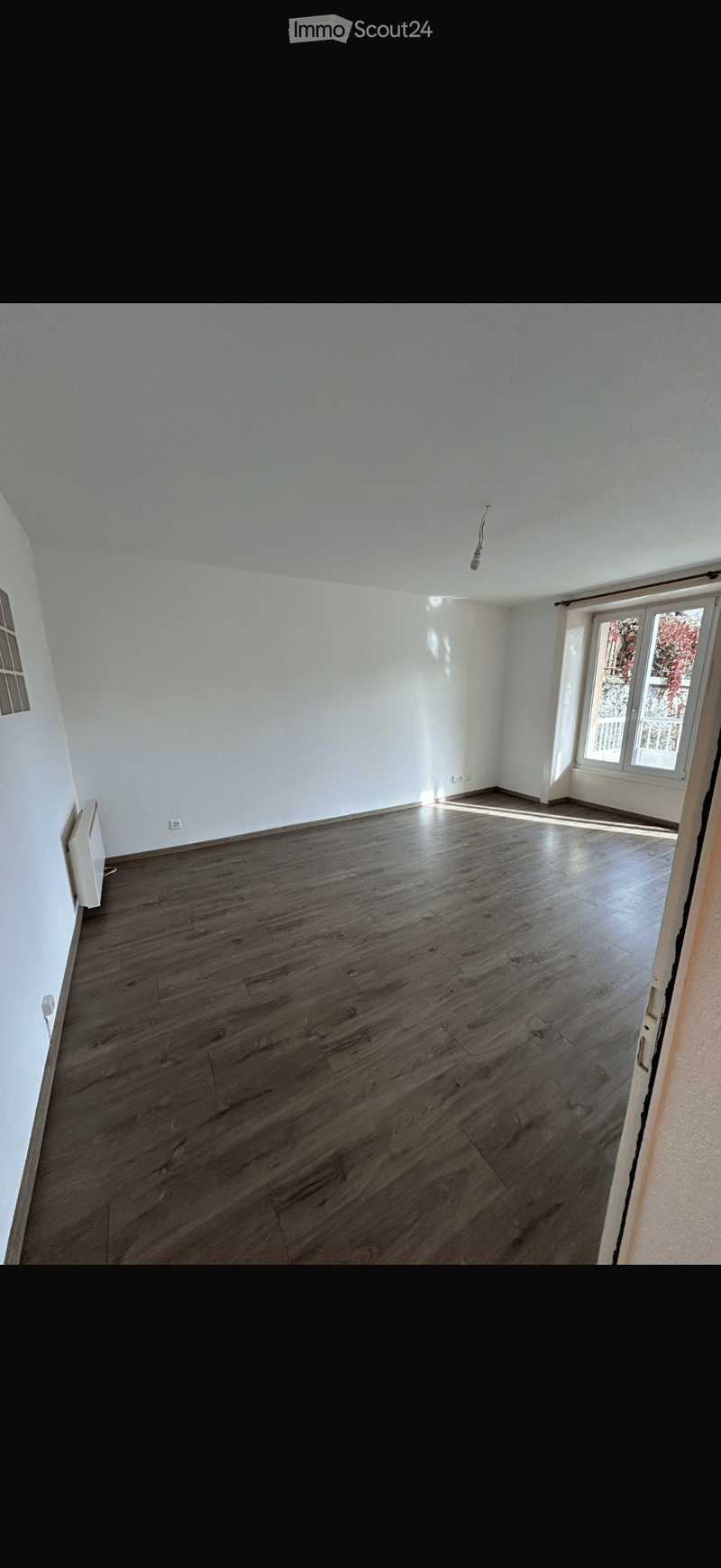 Empty room with wooden flooring, white walls, and large windows allowing natural light to enter.
