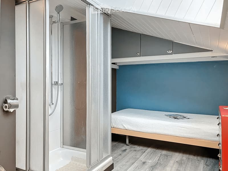 Compact room with a bed, shower, and built-in cabinet. Features a modern design with a glass shower enclosure and a sleek, minimalist aesthetic.