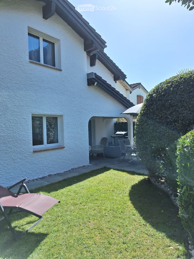 A well-maintained garden area with a lawn, a lounge chair, and a covered patio with outdoor furniture and a grill.
