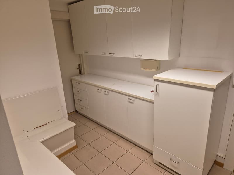 Empty kitchen with white cabinets, tiled floor, and a countertop. No appliances or furniture are present.