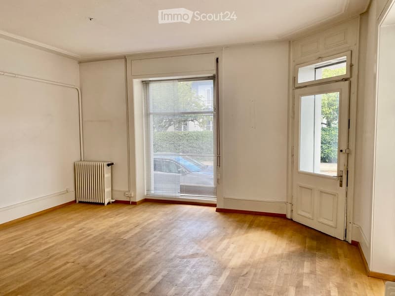 Empty room with wooden flooring, white walls, a radiator, and two windows with blinds.