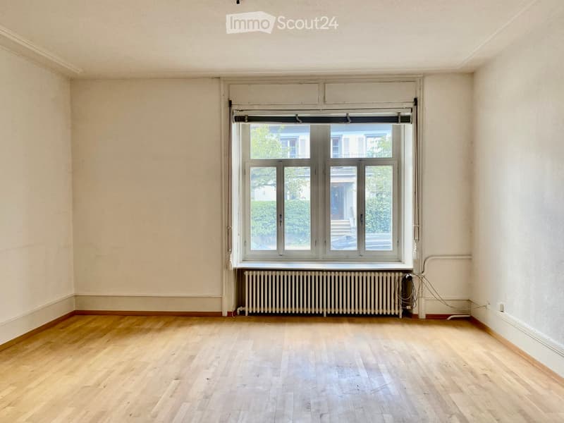 Empty room with wooden flooring, white walls, and a large window with a radiator below it.