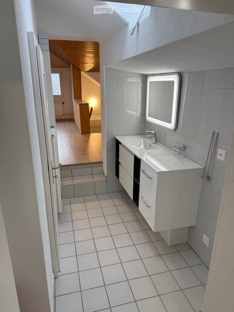 Bathroom with white tiles, white vanity, double sink, mirror, wooden ceiling, wooden floor, power outlet, and a small window.