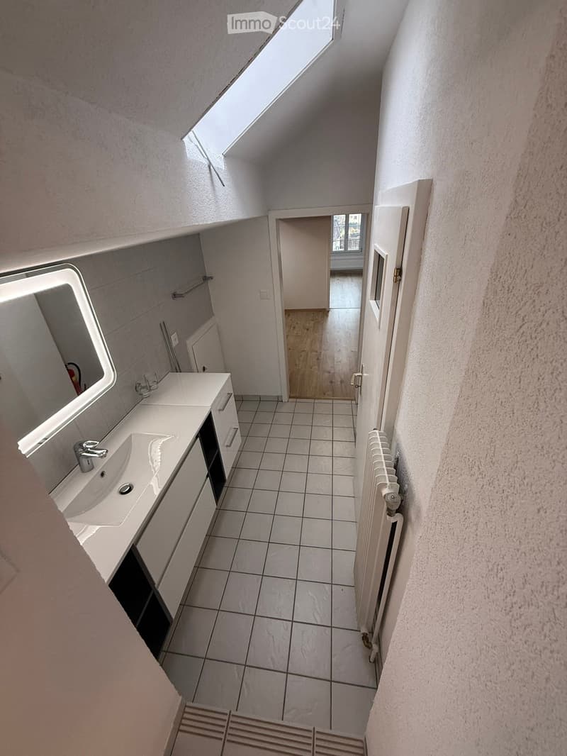 Bathroom with white tiles, white sink, mirror, radiator, and a skylight