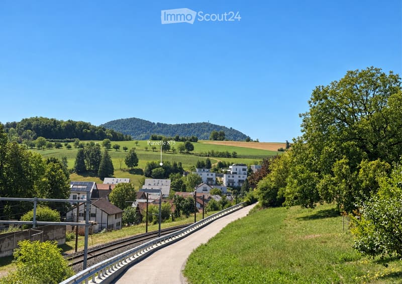 A scenic view of a rural landscape with scattered houses, green fields, trees, and a train track running through the area.
