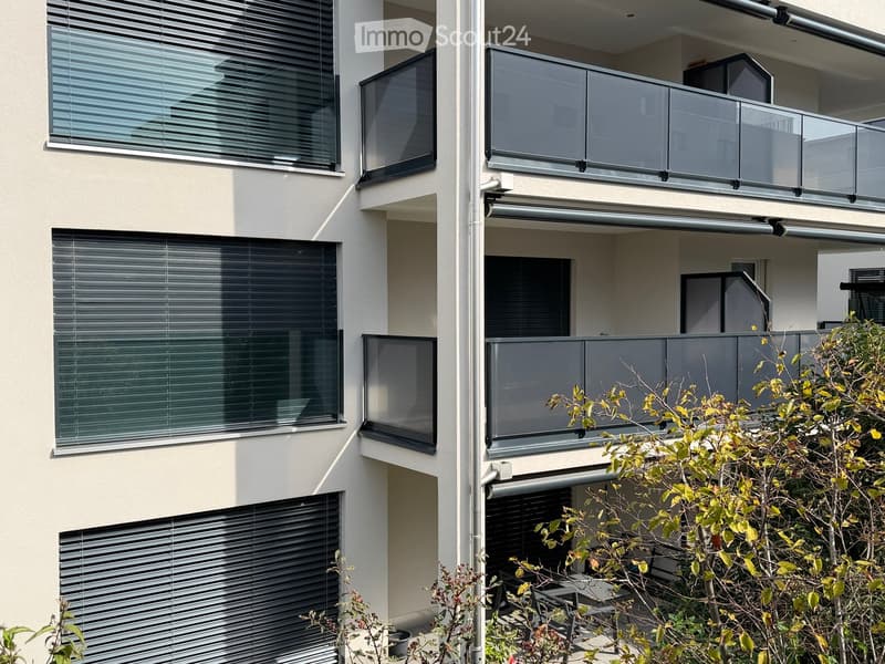 Modern multi-story building with large windows, glass balconies, and sleek blinds.