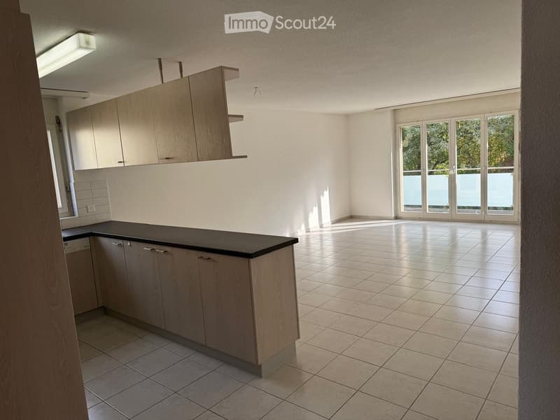 Empty kitchen with light wood cabinets, black countertop, tiled floor, and large windows leading to a balcony.