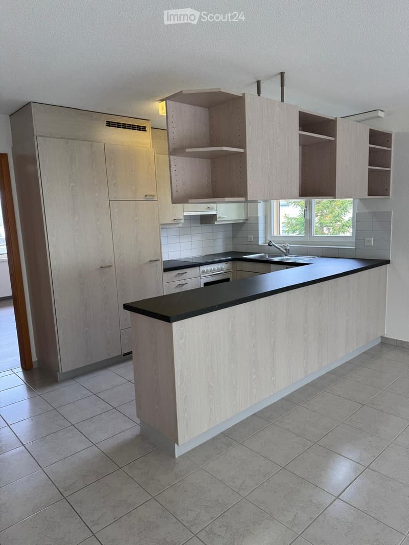 Modern kitchen with light wood cabinets, black countertop, tiled floor, and built-in appliances including a sink, faucet, and oven.