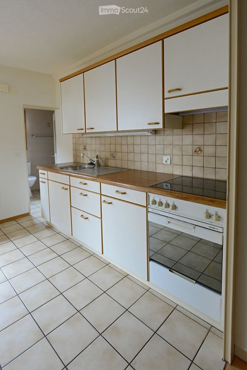 Modern kitchen with white cabinets, wooden countertops, and tiled backsplash. Features a sink, faucet, and built-in oven.