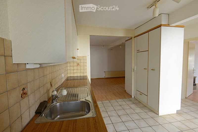 Empty kitchen with wooden cabinets, tiled backsplash, and a stainless steel sink. The space is unfurnished with no appliances or furniture visible.