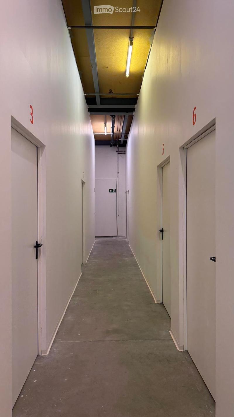 A clean, well-lit hallway with white walls, concrete floor, and numbered doors on both sides.