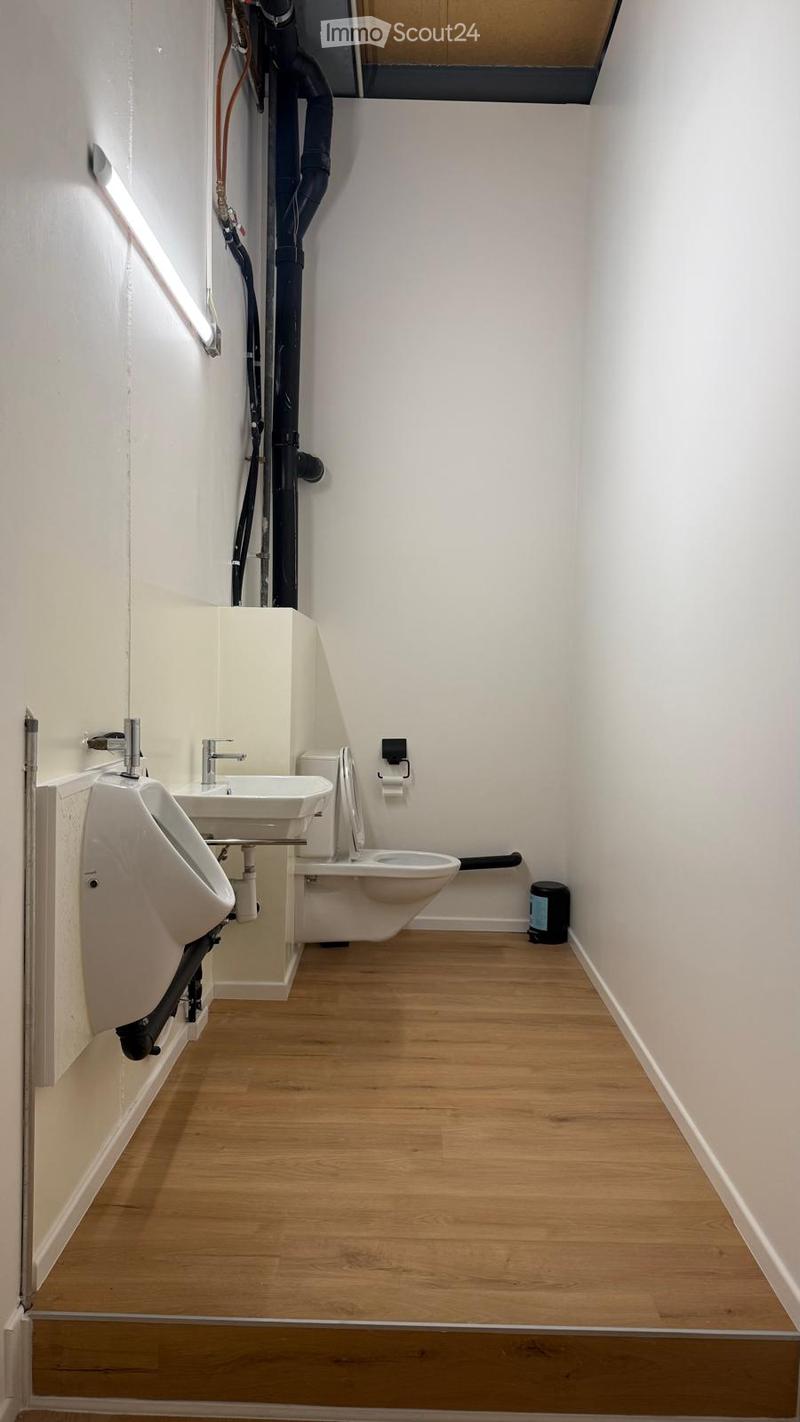 Modern bathroom with wooden flooring, white walls, urinal, sink, toilet, and a mirror above the sink.