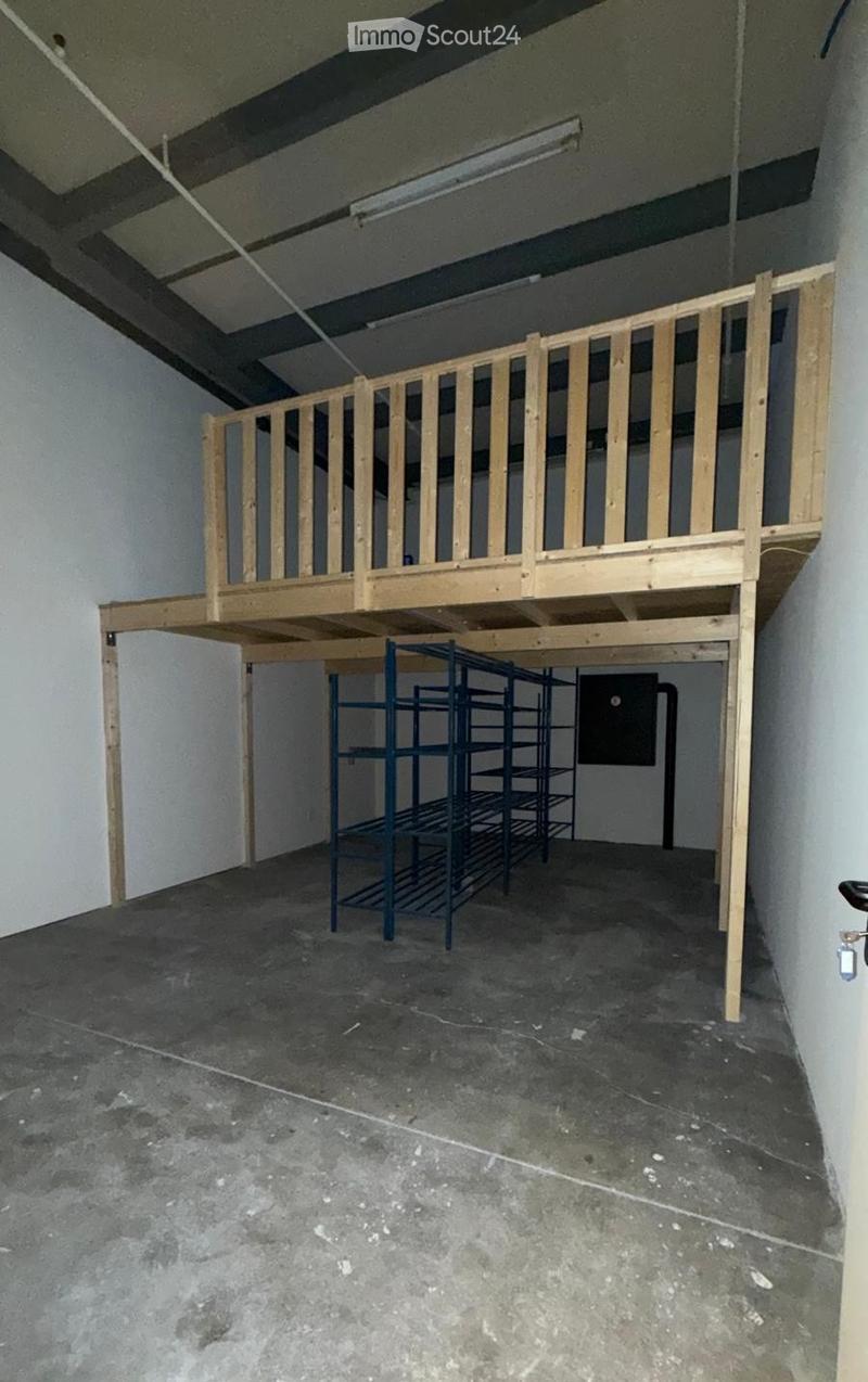 Empty room with a concrete floor, white walls, and a wooden loft platform with a railing. A metal shelving unit is positioned against one wall.