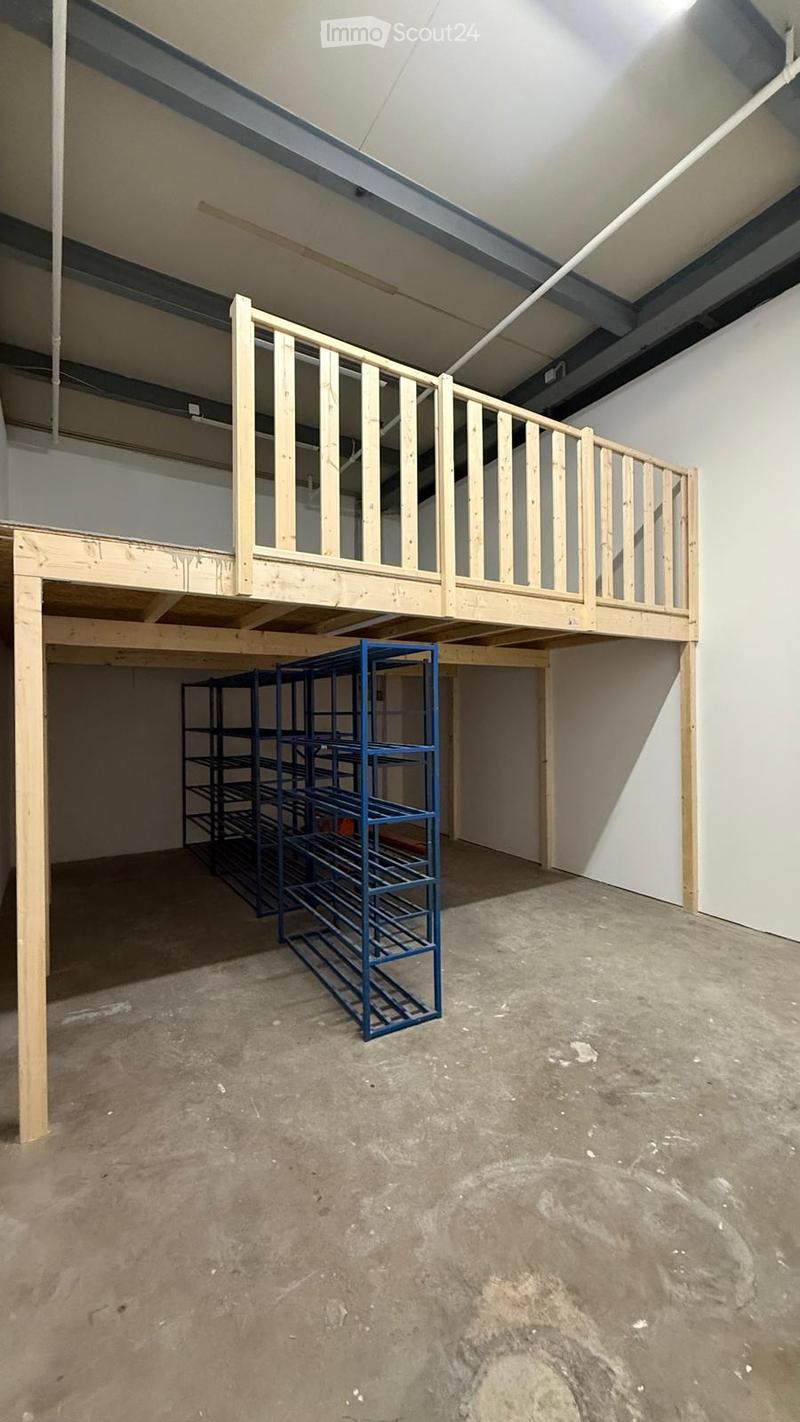 Empty room with unfinished concrete floor, exposed wooden beams, and a metal shelving unit in the corner. The room features a wooden loft platform with a railing.