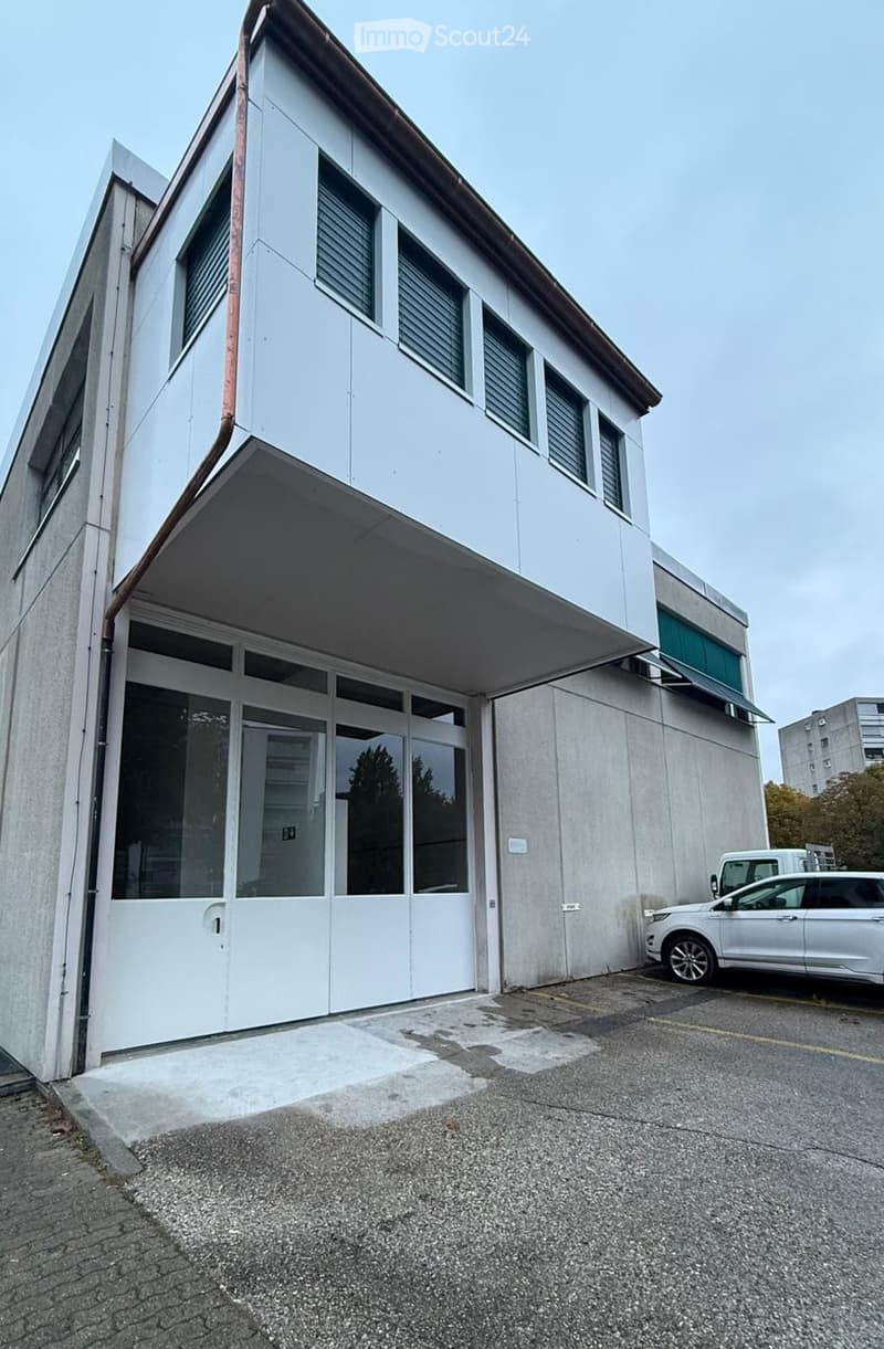 Modern two-story building with white facade, large windows, and a covered entrance area. A white SUV is parked nearby.