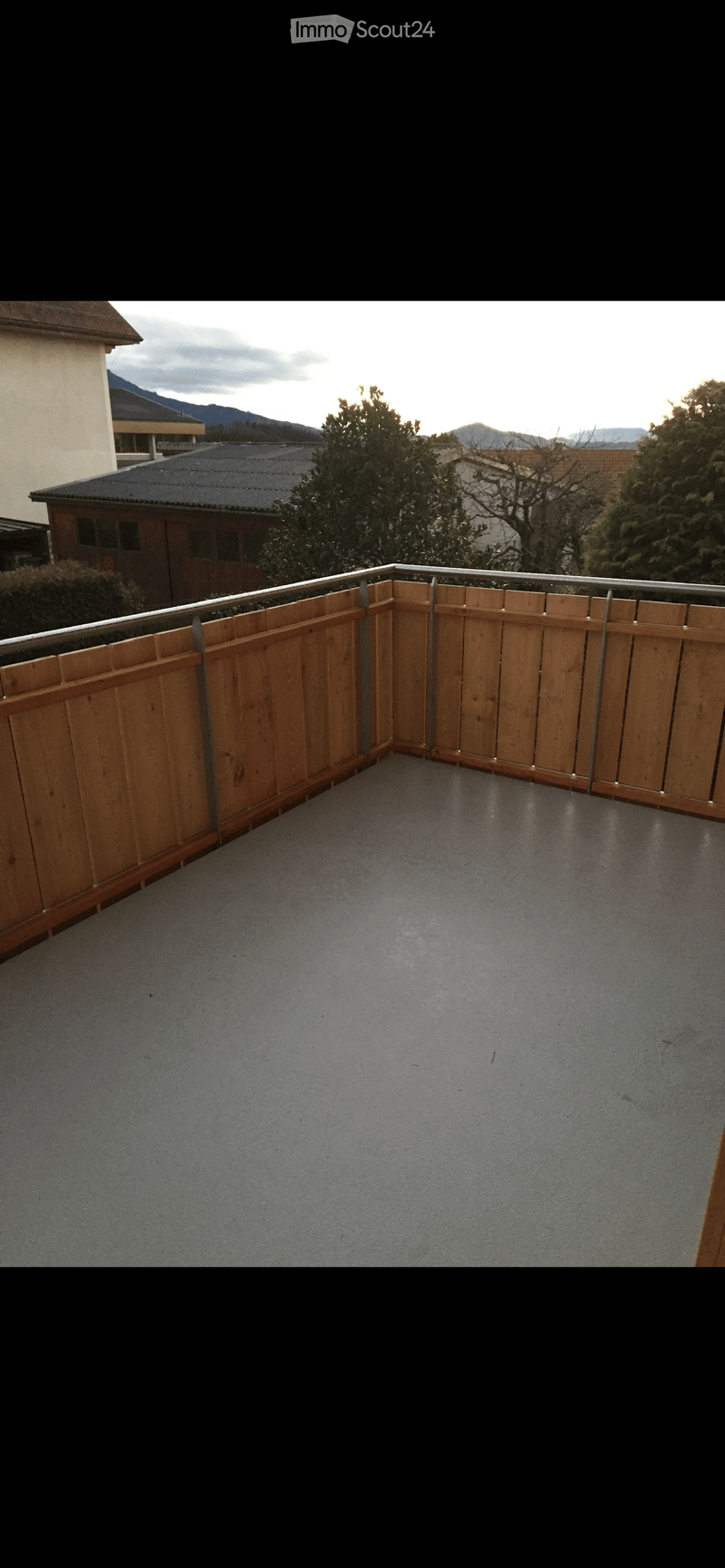 Balcony with wooden railings, concrete floor, view of trees and mountains