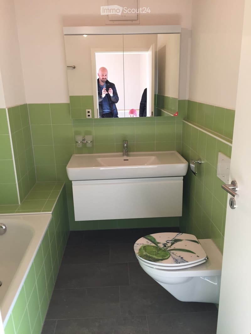 Bathroom with green tiles, white sink, white toilet, bathtub, mirror, power outlet
