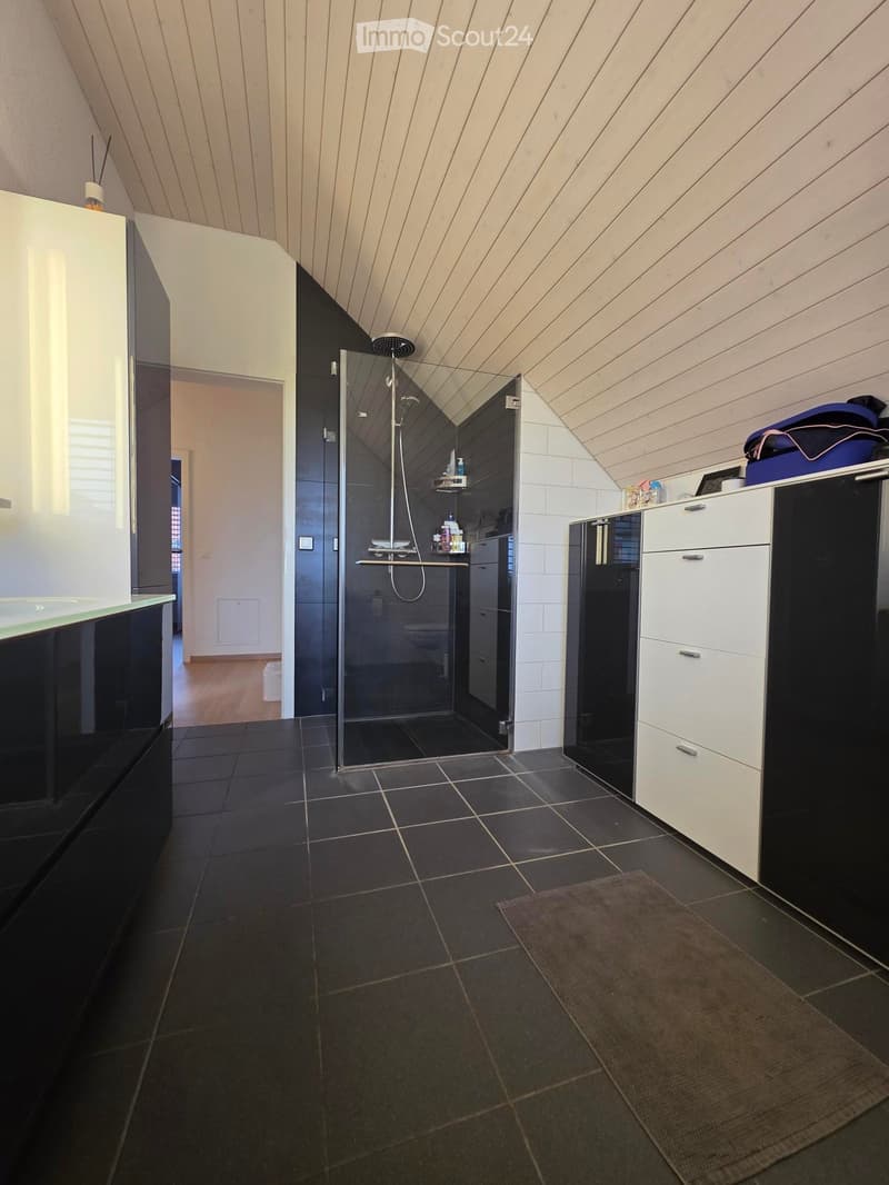 Modern bathroom with black tiles, a glass-enclosed shower stall, a white and black cabinet, and a small rug on the floor.