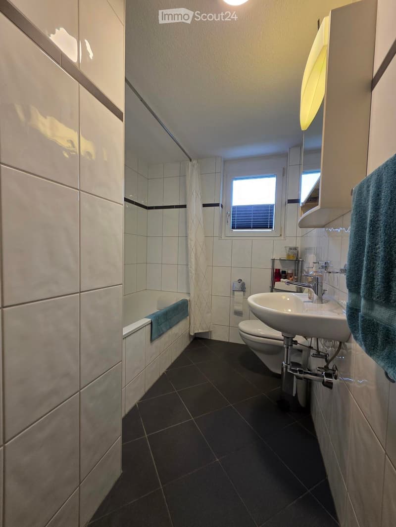 Modern bathroom with a bathtub, sink, toilet, and mirror. Features dark tiled flooring and white tiled walls.