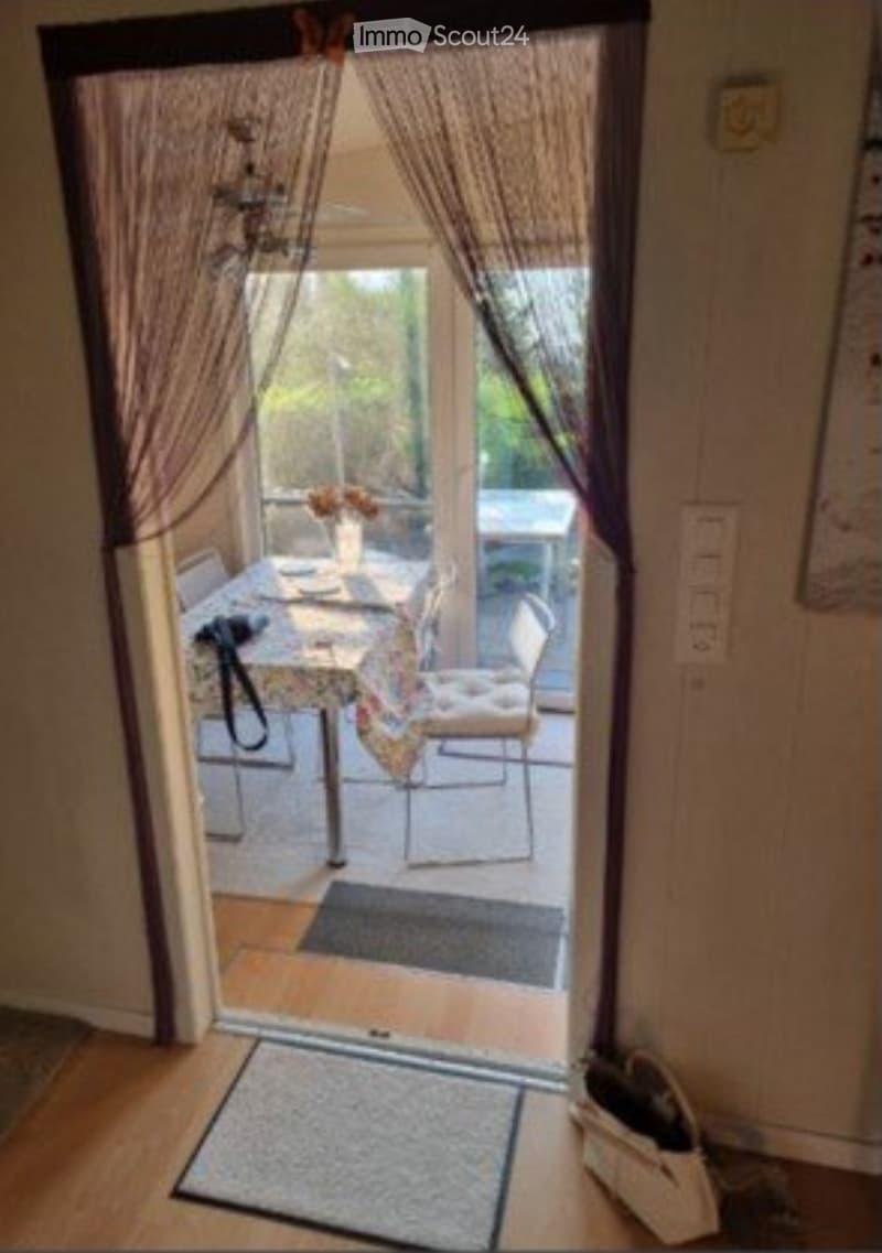 A room with a sliding glass door leading to a balcony or terrace area, furnished with a small table and chairs, and a vase with flowers on the table.