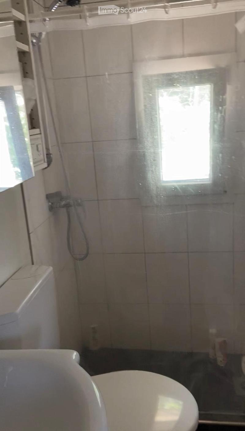 Bathroom with a toilet, bathtub, and a shower area with a glass door. The walls are tiled, and there is a window providing natural light.