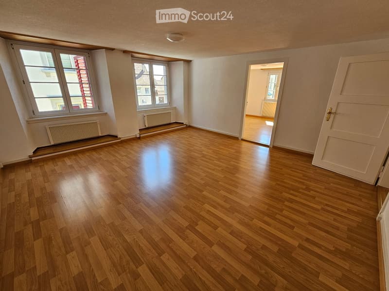 Empty room with wooden flooring, large windows, and a door leading to another room.