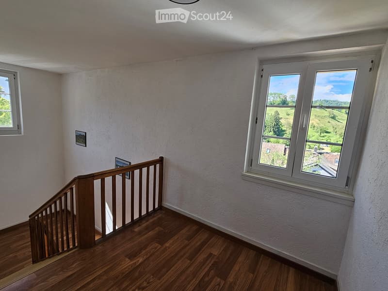Staircase with wooden steps and railing, white walls, large windows offering a view of the landscape, and framed pictures on the wall.