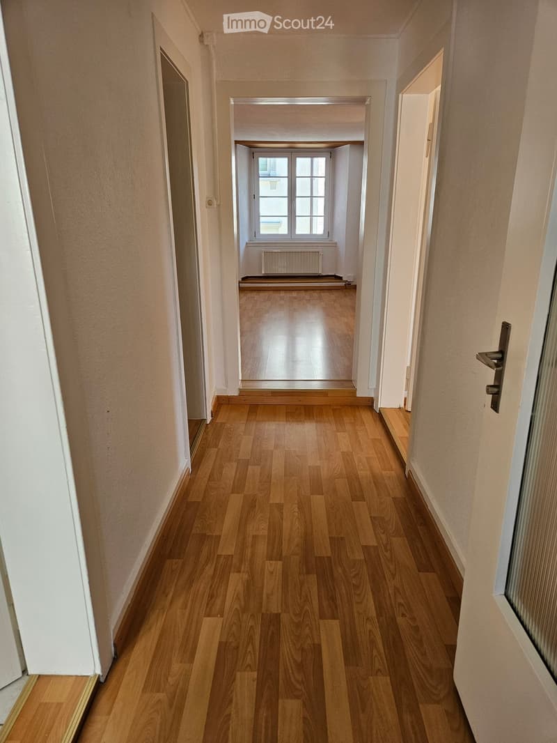 Empty hallway with wooden flooring, white walls, and multiple doors leading to other rooms.