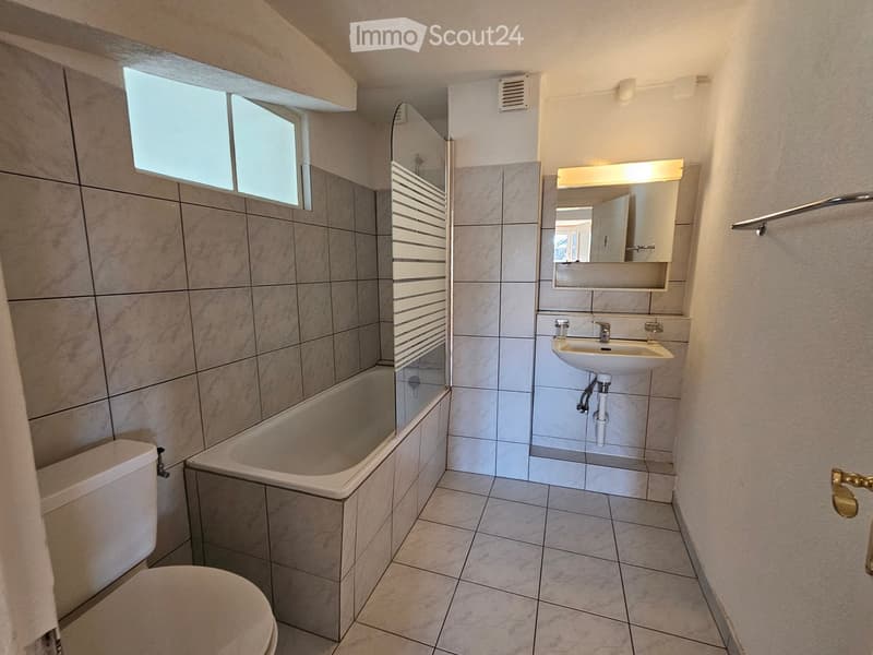 Modern bathroom with tiled walls and floor, featuring a bathtub, toilet, sink, and mirror.