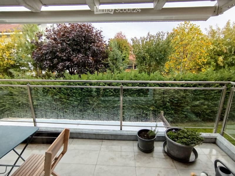 Balcony with a glass railing, tiled floor, and outdoor furniture including a table, chair, and potted plants.