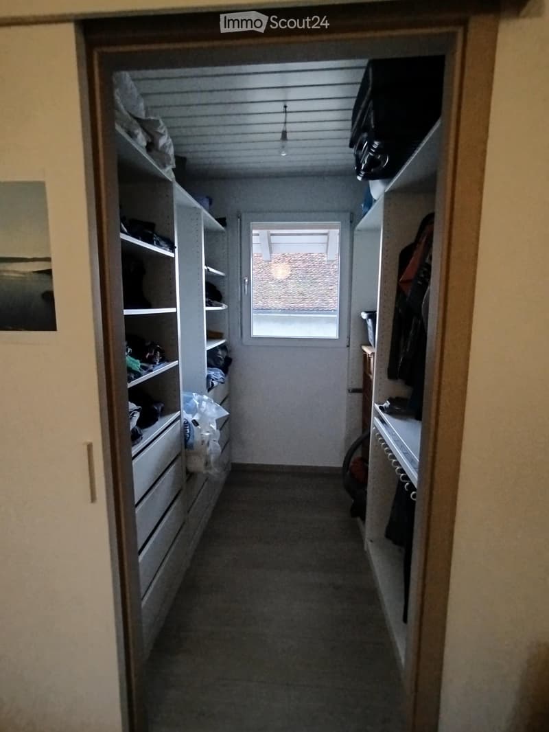 A narrow hallway with built-in storage units on both sides, a small window at the end, and a light fixture hanging from the ceiling.