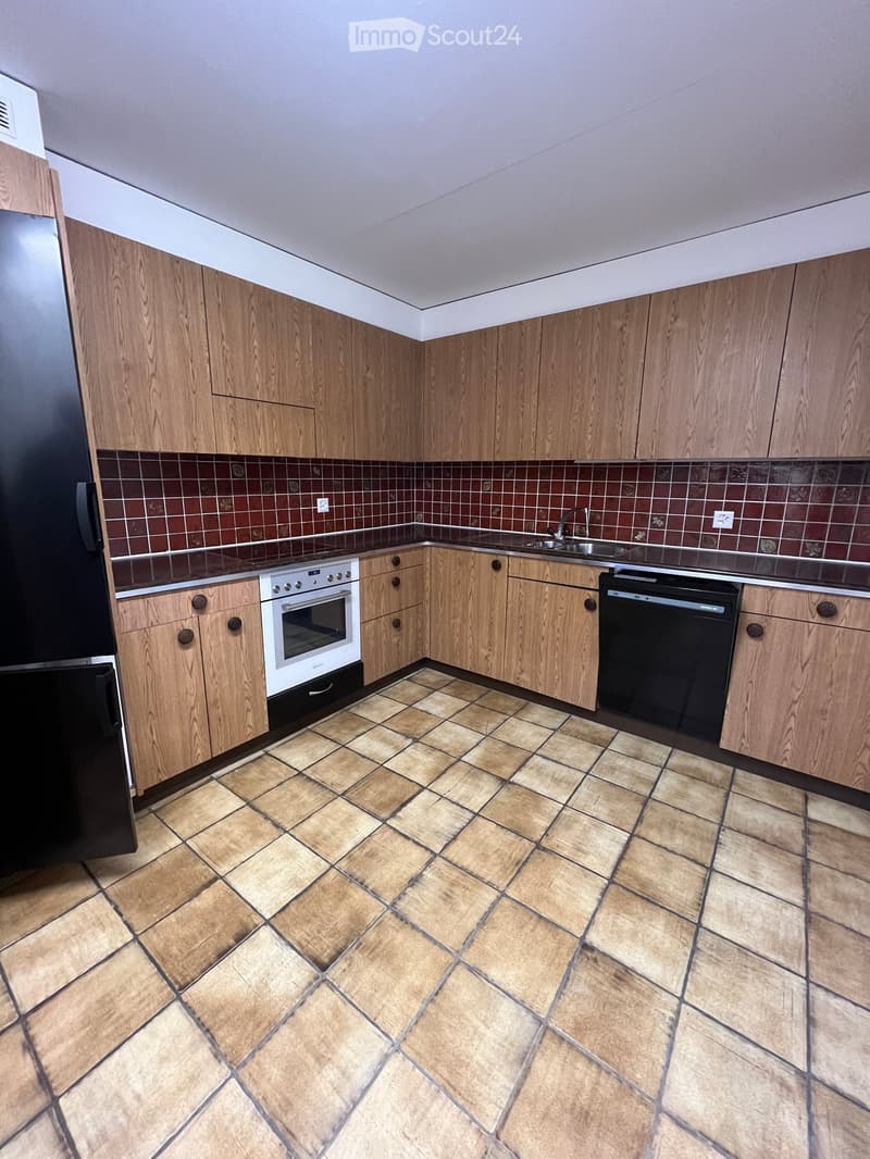 Modern kitchen with wooden cabinets, tiled backsplash, and tiled floor. Features an oven, dishwasher, and sink.