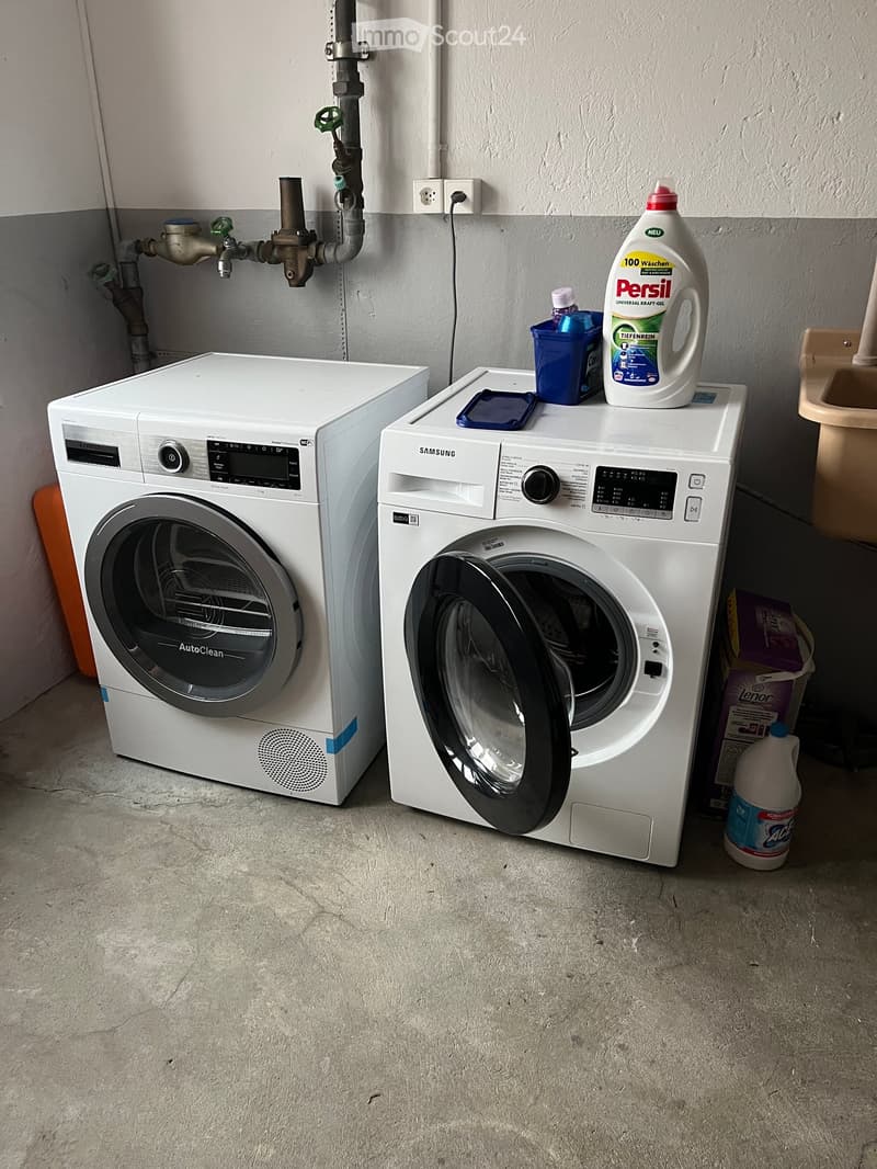 A bathroom with a washing machine and dishwasher, along with various cleaning supplies and detergent bottles placed on top of the appliances.